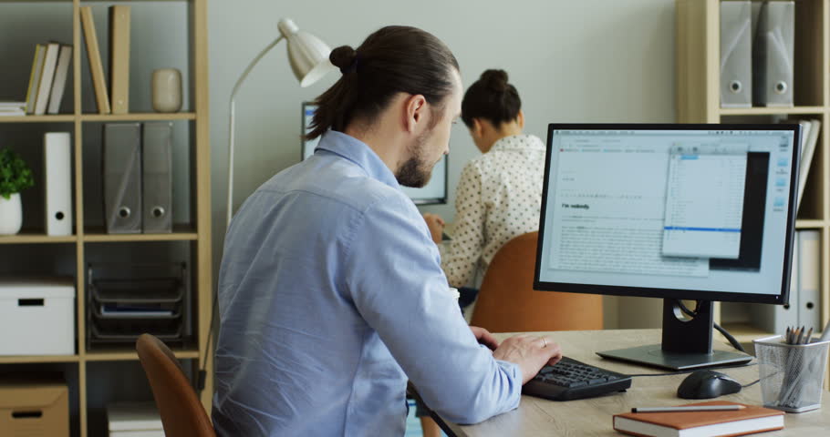 Young handsome man working on the computer at his office and it being broken with error writing on the screen, then taking his smartphone and taping on it. Indoor.