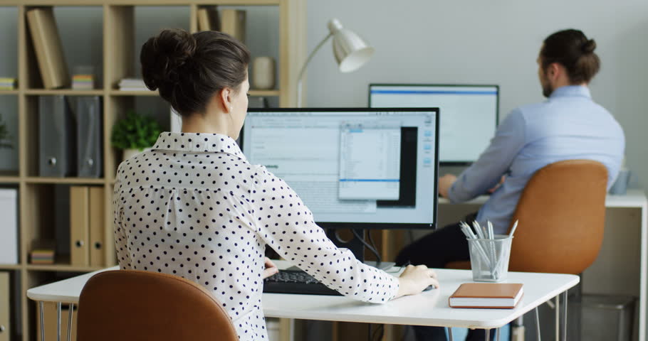 Rear of the Caucasian young woman stopping working at the computer as there being error writing on its screen. At the office. Inside.