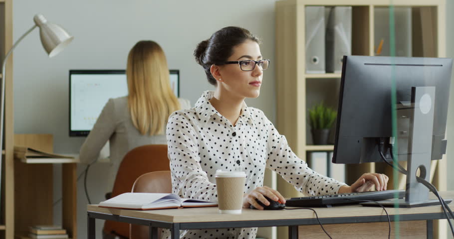 Young pretty brunette woman working at the laptop computer in the office, then smiling ang going away with her stuff. Inside.