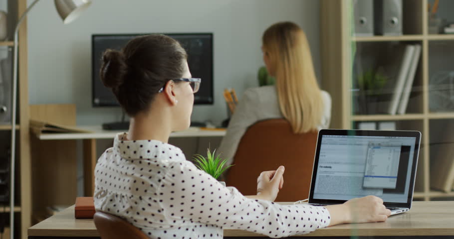Rear of the caucasian young female office worker sitting at her table in the office and using laptop computer wich being broken and there being error on the screen. Indoor.