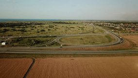Summer aerial drone footage of transport junction, traffic cross road junction day view from above with green tree circle road, near is a wheat field. Top down view of traffic jam.