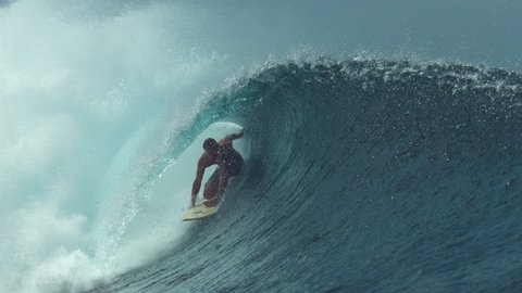 SLOW MOTION, CLOSE UP: Pro surfer drags his hand through the water while surfing a beautiful tube wave glimmering in the bright sunshine. Young surfboarder gets almost swept by a big barrel wave.