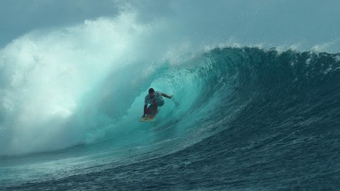 SLOW MOTION, CLOSE UP: Pro surfboarder rides a big tube and drags his hand through the spectacular crystal clear ocean water. Sportsman on vacation having fun surfing in stunning Teahupoo, Tahiti.