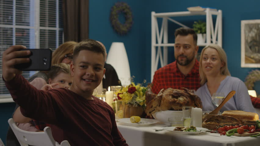 Teen boy sitting with parents and grandparents and sister at table on Thanksgiving day and taking selfie together using smartphone Royalty-Free Stock Footage #1013287757