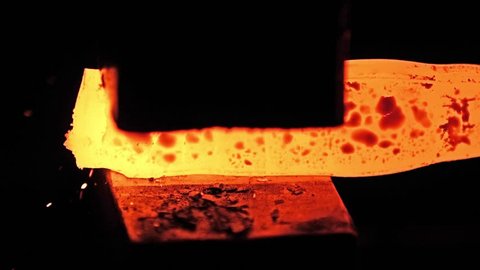 Shaping of red hot metal part on the anvil with a jackhammer pneumatic mallet in blacksmith workshop