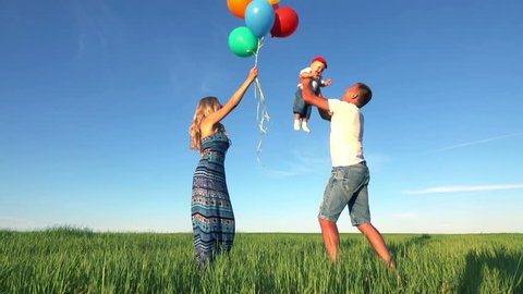 A young family playing in nature on a Sunny day. Father at a slow pace throws the baby and catches it. Woman with balloons. The concept of a happy family. Slow motion.