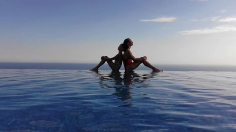 Two girls are sitting on the edge of an infinity pool