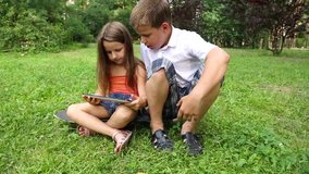 Sister and brother play on the tablet in the park