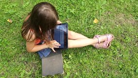 Little girl prints words on a tablet while sitting on a skateboard