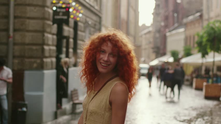 attractive woman with red curly hair walking in the rain on the street look at camera spinning happy smile cute fashion water silhouette summer face female lonely stop close up Royalty-Free Stock Footage #1013312201