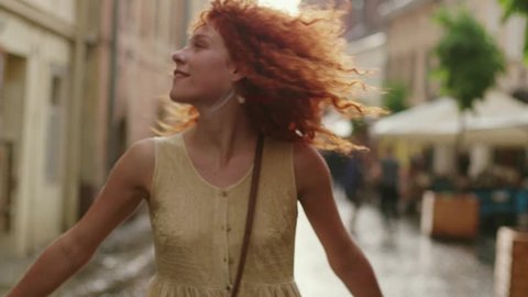 Stylish attractive woman with red curly hair walking in the rain on the street look at camera spinning happy smile cute fashion water silhouette summer face female lonely stop close up