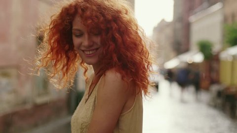 Cute woman with red curly hair walking in the rain on the street look at camera spinning happy smile beautiful portrait fashion water silhouette summer face female lonely stop close up
