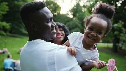 Portrait young african father hugging his daughter play holds on hands twists spending holiday together in park family affection smile slow motion child summer man kid sun girl parenting outdoors