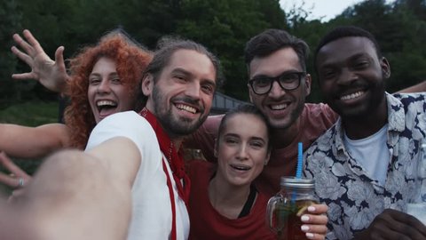 Close up happy multi-ethnic friends doing selfie together look at camera talk drink beer barbecue for summertime dinner party girl couple rest woman man nature play guitar sunset slow motion portrait