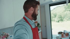Attractive bearded vloger records room-tour video about his modern light kitchen, tastes sweet red pepper, invites his wife with a cute child to greet the subscribers. Food vlog, modern parents.