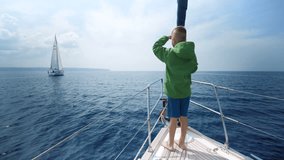 Little boy stands on the bow of the yacht and shows the way