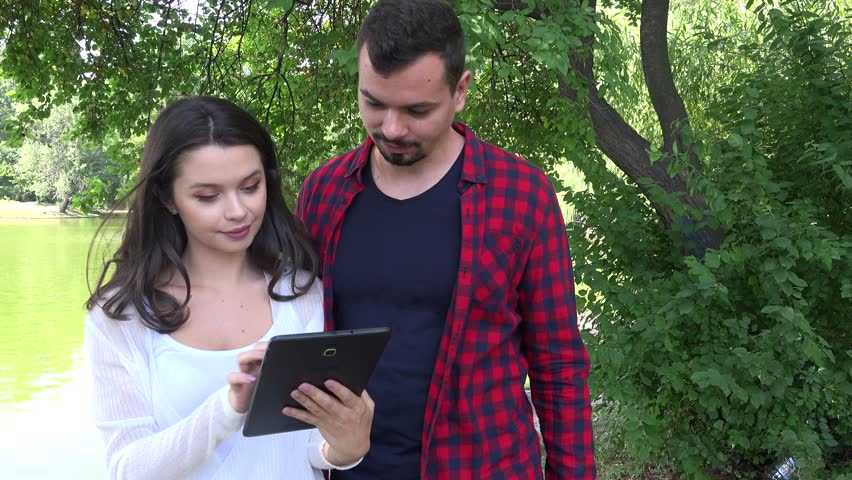 Beautiful young couple in nature playing on digital tablet emotional friendship 