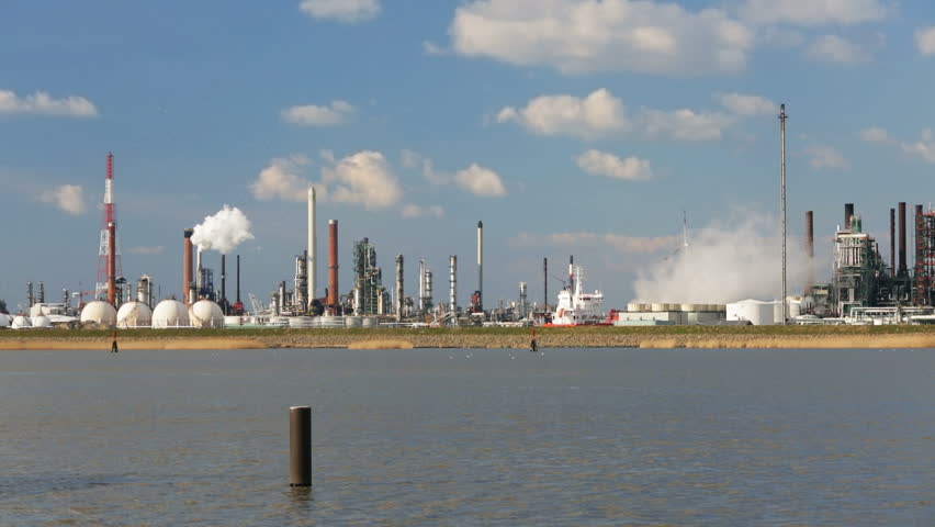 A large oil refinery in the harbor of Antwerp, Belgium with perfect blue sky and the Scheldt River in the foreground.
