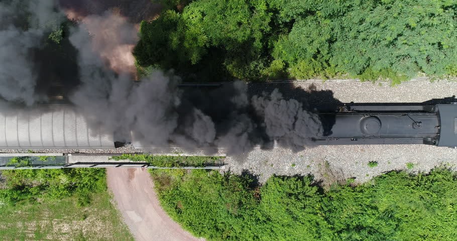 Aerial view of steam train running on the tracks in the countryside. Heritage historic steam locomotive with black smoke seen from above by drone.