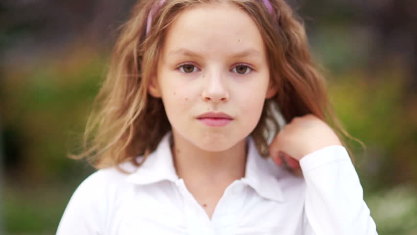 Closed portrait of a young schoolgirl. The girl calmly looks at the frame, straightens her hair. Curly hair, brown eyes, natural beauty