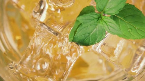 Slow motion yellow drink beautifully pour into a glass with ice and mint leaves top view close-up