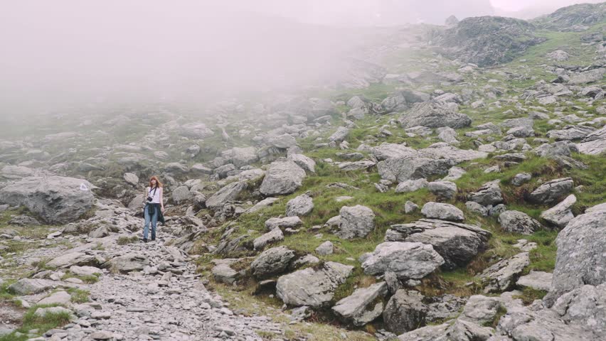 A young woman hiker climbs mountains with photo camera. Transfagarasan, Carpathian mountains in Romania