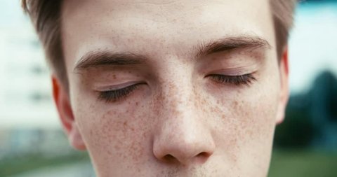 Close-up view of the guy with freckles opening his green eyes and looking at camera. 4k footage.