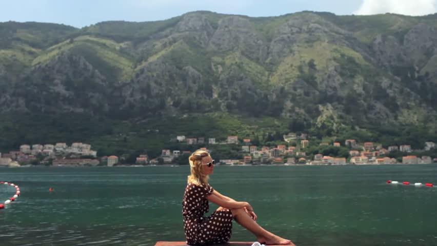beautiful woman in a summer dress resting on a dock in the background of the mountains