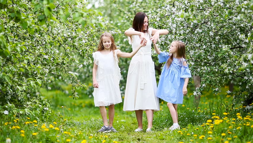 Adorable little girls with young mother in blooming cherry garden on beautiful spring day