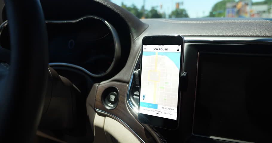 A smartphone attached to the dash on a vent holder in a moving car shows an ETA to the ride sharing destination. App screen simulated.  	 Royalty-Free Stock Footage #1013367809