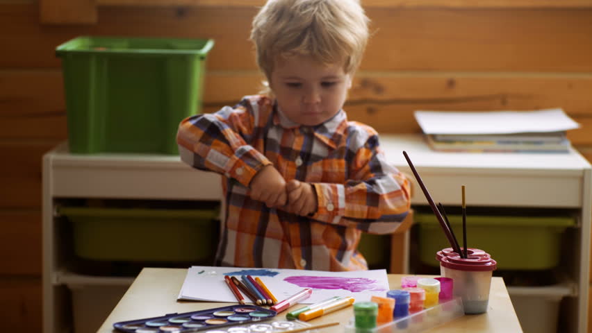 Child drawing picture with paitint in album using a lot of painting tools. Creativity concept.