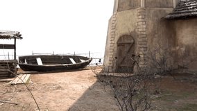 Old dilapidated black wooden boat with a one-storey house, a well and a hill in Russian Cossack village. Video.  Abandoned northern village.
