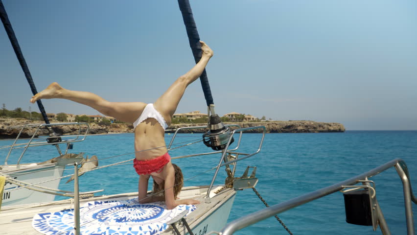 Close-up Shot of a Fit Young Woman Doing Yoga on a Sailing Yacht. In the Background Beautiful Calm Sea and Clear Sunny Sky Royalty-Free Stock Footage #1013396753