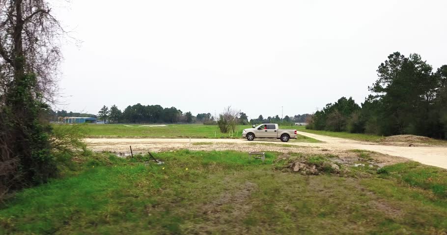 Aerial Chase of Tan Ford F150 Pickup on gravel road. Chasing beside the truck at about 100 to 200 feet distance and keeping pace with it. Drone is low to the ground.
