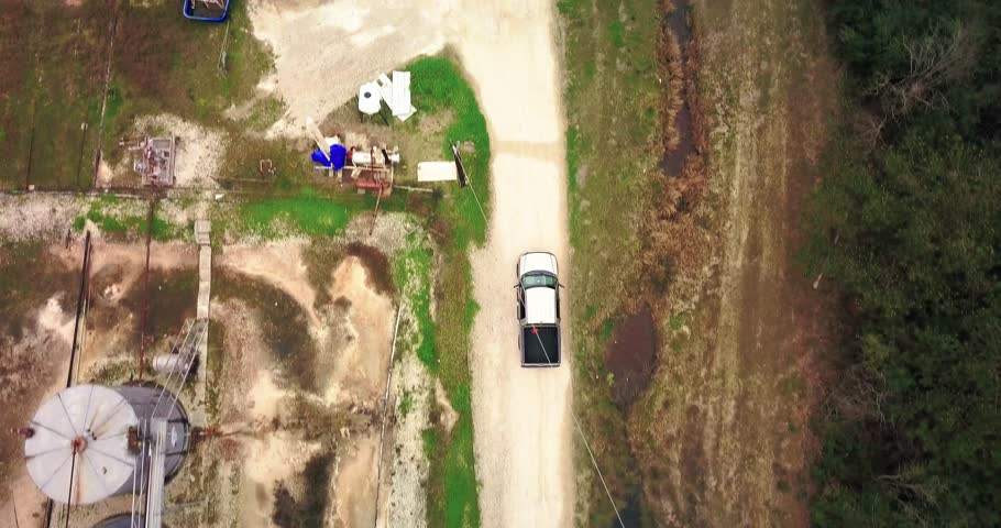 Aerial Chase of Tan Ford F150 Pickup on gravel road. 150 feet over the truck as it passes a water treatment plant.