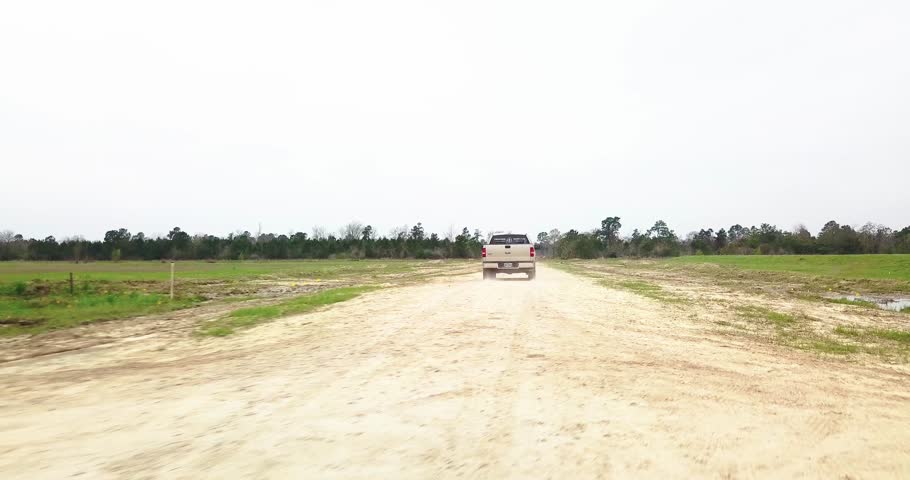 Aerial Chase of Tan Ford F150 Pickup on gravel road. Chasing behind the truck at about 100 to 200 feet distance and low to the ground.