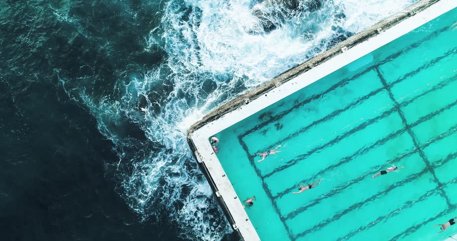 Swimming pool at Bondi Beach, Australia. Aerial shot looking directly down at a section of the pool with swimmers and waves crashing. Royalty-Free Stock Footage #1013400863