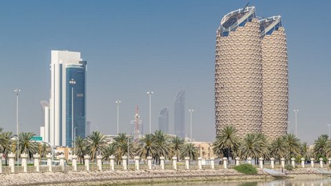 ABU DHABI, UAE - CIRCA MARCH 2018: View of skyscrapers skyline with Al Bahr towers in Abu Dhabi timelapse. Reflections on water and palms on the street. United Arab Emirates