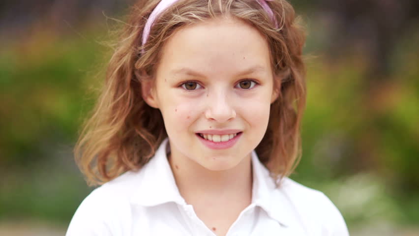 Close up of a little blonde brown-eyed cute girl face. Girl blinking her eyes and smiling. Inside. Portrait shot. Happy schoolgirl