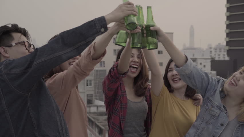 Slow motion - Group of young asian women and man people dancing and raising their arms up in air music played by dj at sunset urban party on rooftop. Young asian friends hanging out with drinks beer.