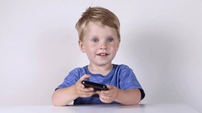 Little kid boy with mobile phone in hands, looking in it and talking on white background