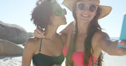 Two beautiful friends taking selfies giving kiss on cheek on the beach on summer vacation wearing bikinis RED DRAGON