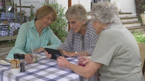 Group of senior women looking at photos on a tablet computer at an outdoor restaurant