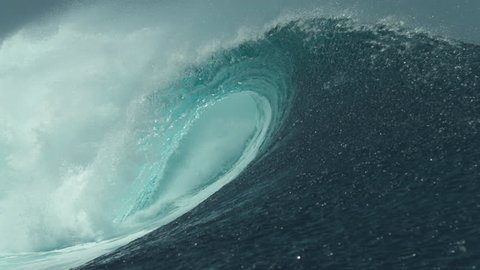 SLOW MOTION, CLOSE UP: Crystal clear ocean water glistens in the bright tropical sunshine while a large tube wave crashes near a remote island in French Polynesia. Picturesque big glassy barrel wave.