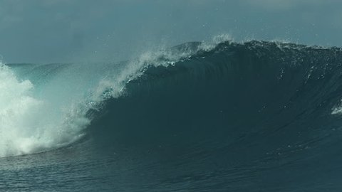 SLOW MOTION CLOSE UP: Powerful glistening barrel wave surges past a popular surf spot in stunning Teahupoo, Tahiti. Amazing view of a tube wave raging from the Pacific and towards remote exotic island