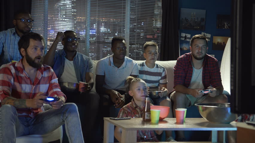 Group of multiethnic men and teens gathering on sofa at home and playing videogame with gamepads | Shutterstock HD Video #1013428349
