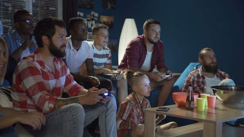 Group of multiethnic men and teens gathering on sofa at home and playing videogame with gamepads | Shutterstock HD Video #1013428358