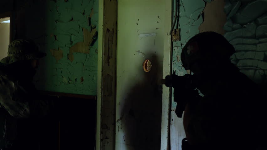 Two soldiers in full gear in an abandoned building clearing the room. Tactical action