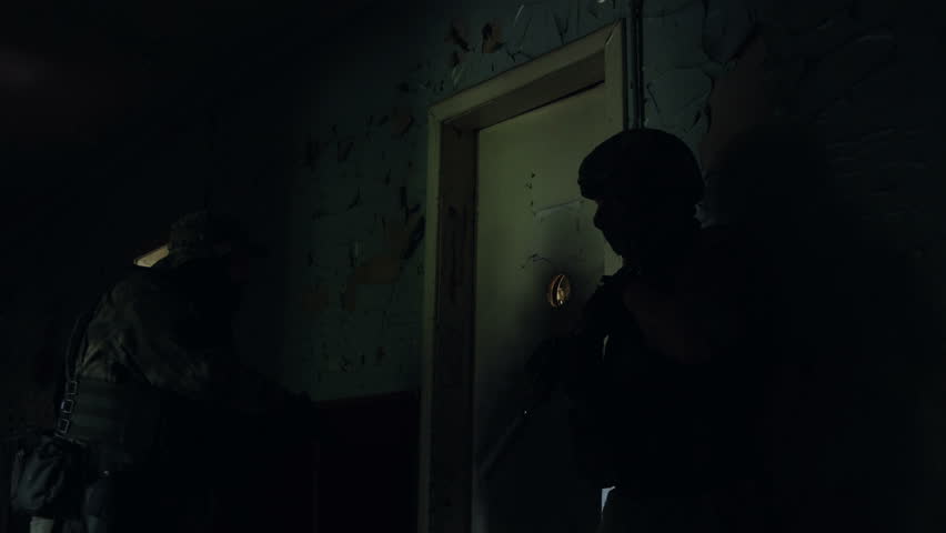 Soldier with a gun opens the door with his feet and enters the room. Second soldier assists