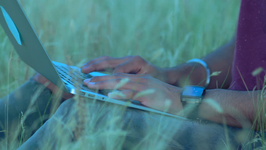 Close-up, Hands of an Indian Paren Sitting on the Grass Typing Text on the Laptop Keyboard
